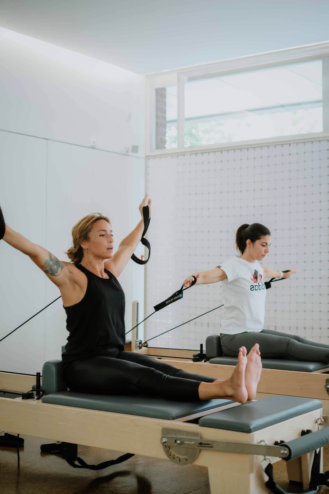 Duas alunas em exercício de braços no Reformer, com a luz natural do estúdio